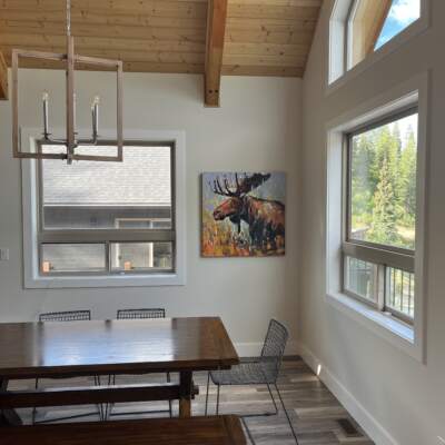 Original moose painting by Verne Busby installed in the dining room of a cozy mountain home with large windows.