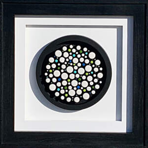 Wood and white and colorful enamel dot mosaic on a black background with a white mat and black frame.